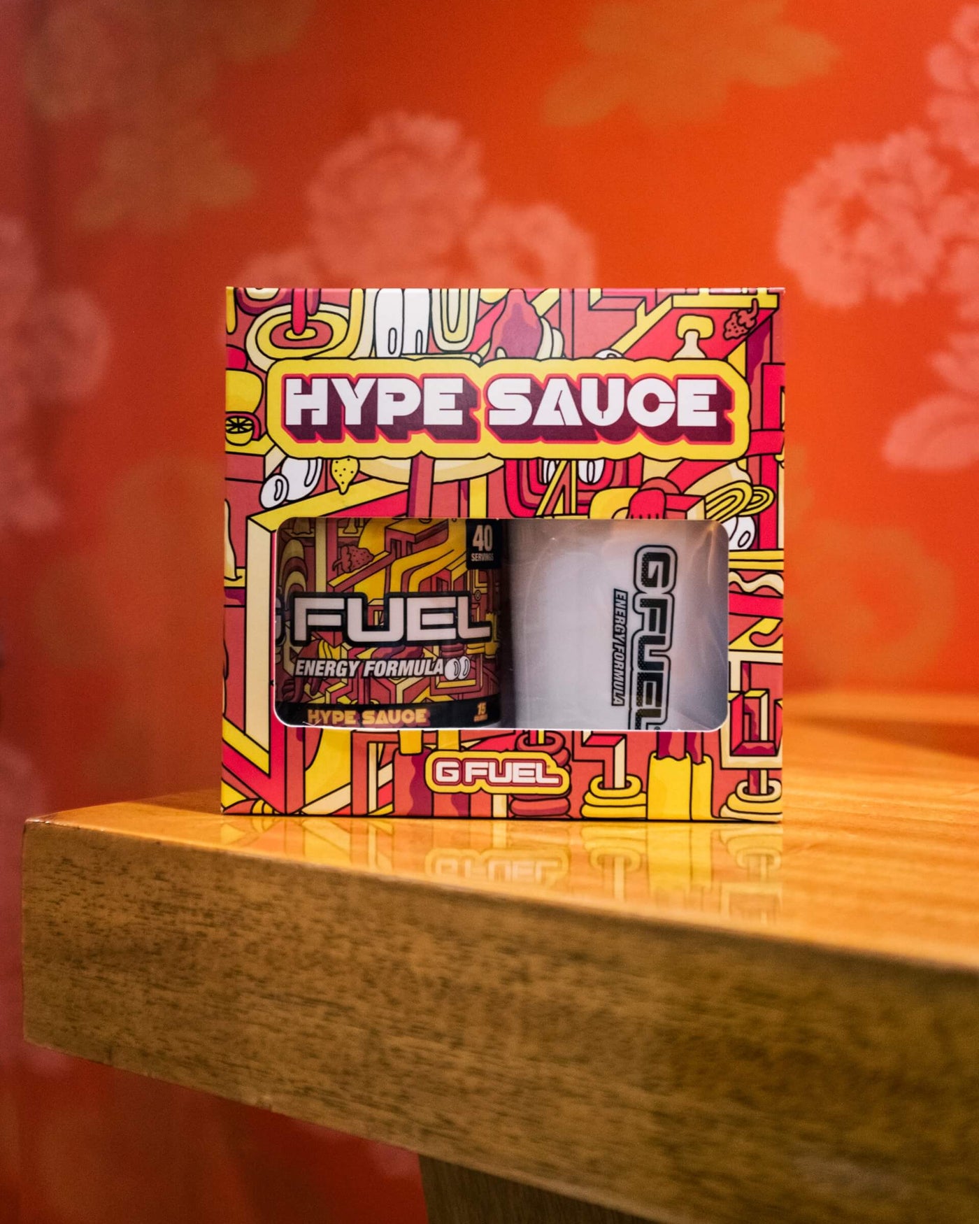 G FUEL HYPE SAUCE collectors box, which includes one HYPE SAUCE tub and one HYPE SAUCE shaker cup, is on a wooden table.