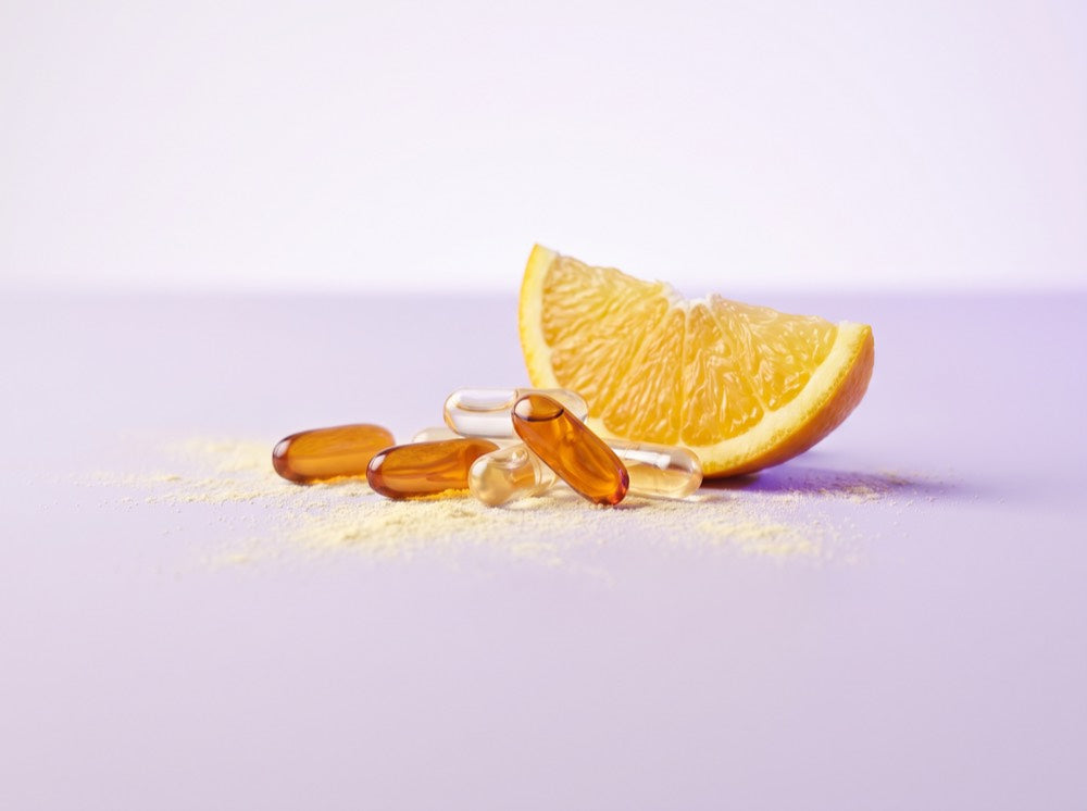 Vitamin capsules and citrus beside a scattering of vitamin powder
